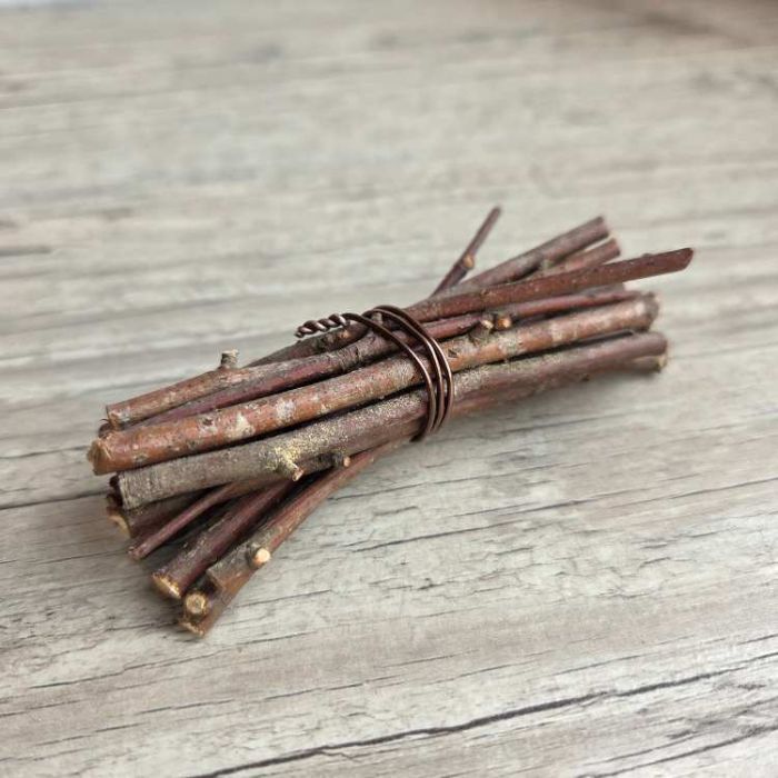 Mini fagot de bois en brindilles naturelles liées d'un fil métallique cuivré, posé sur une table en bois