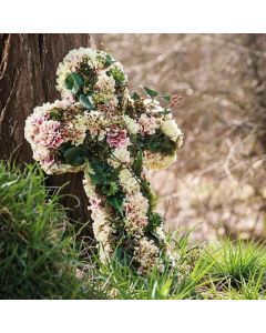 Croix florale de deuil garnie d'&oelig;illets, lierre, baies et joubarbes, pos&eacute;e au pied d'un arbre